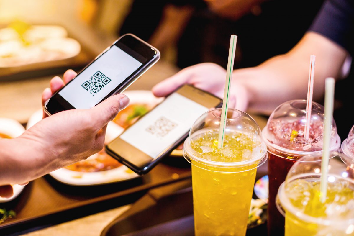 Hand using smart phone to scan QR code on tag with blurry food, dessert and customers in restaurant to accepted generate digital pay without money. Qr code payment concept.
