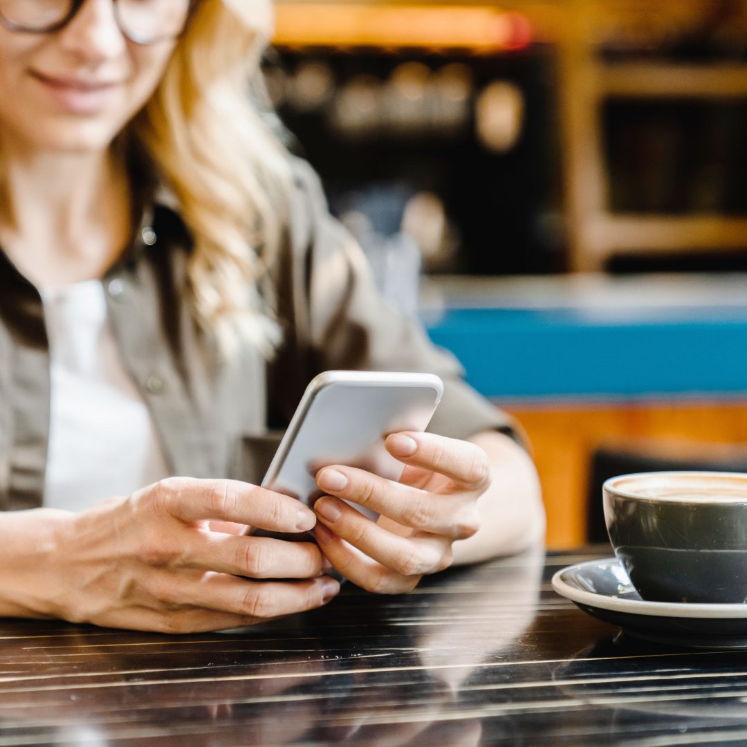 Focused cropped closeup shot of a caucasian young woman holding using smart phone cellphone for e-banking remote work while drinking coffee in cafe restaurant